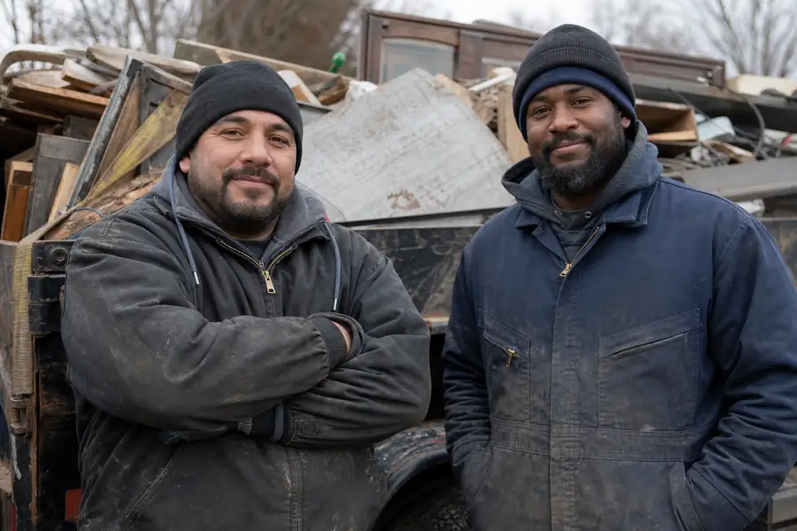 Two junk removal crew members next to a loaded truck