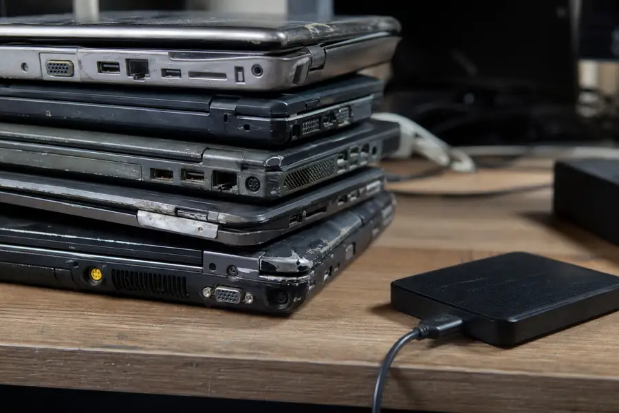Stack of old laptops next to an external drive on a desk