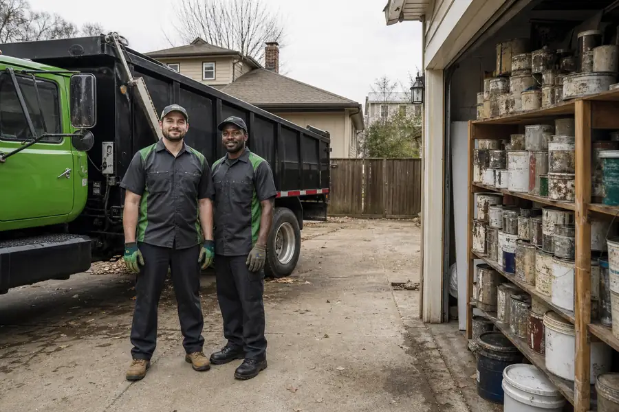 Green-accented junk removal truck with uniformed two-person crew, stack of old paint cans on a garage shelf