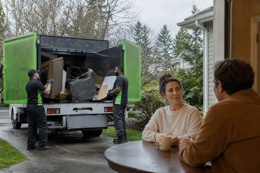 Green-accented junk removal truck with uniformed two-person crew, two people having a calm conversation at a kitchen table