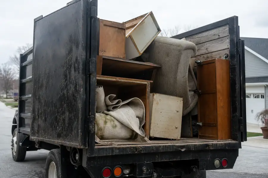 Junk removal truck being loaded with household junk in a suburban driveway