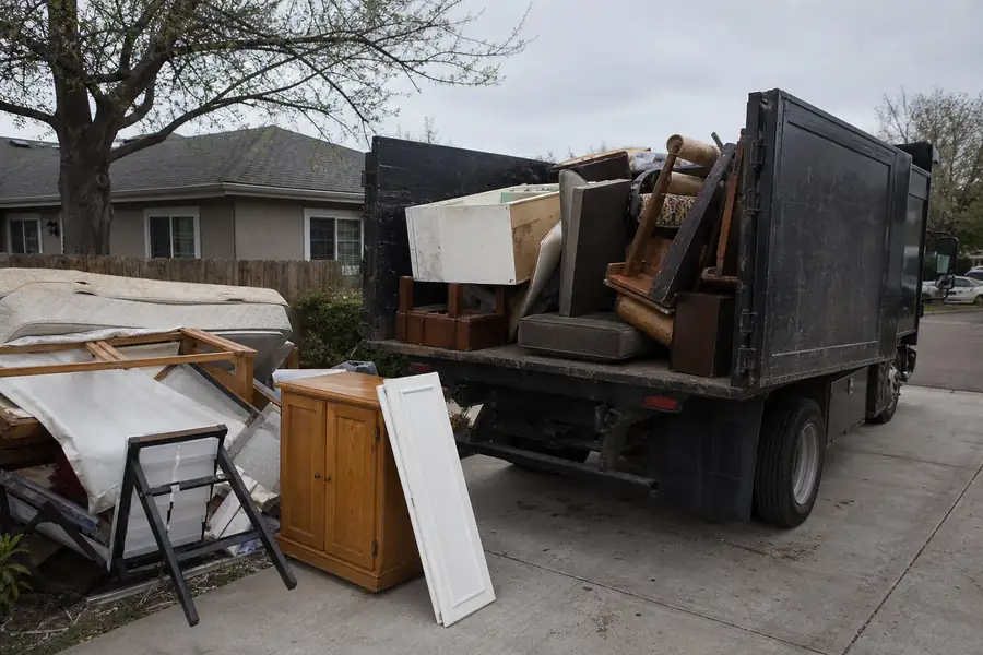 Junk removal truck being loaded with household junk in a suburban driveway