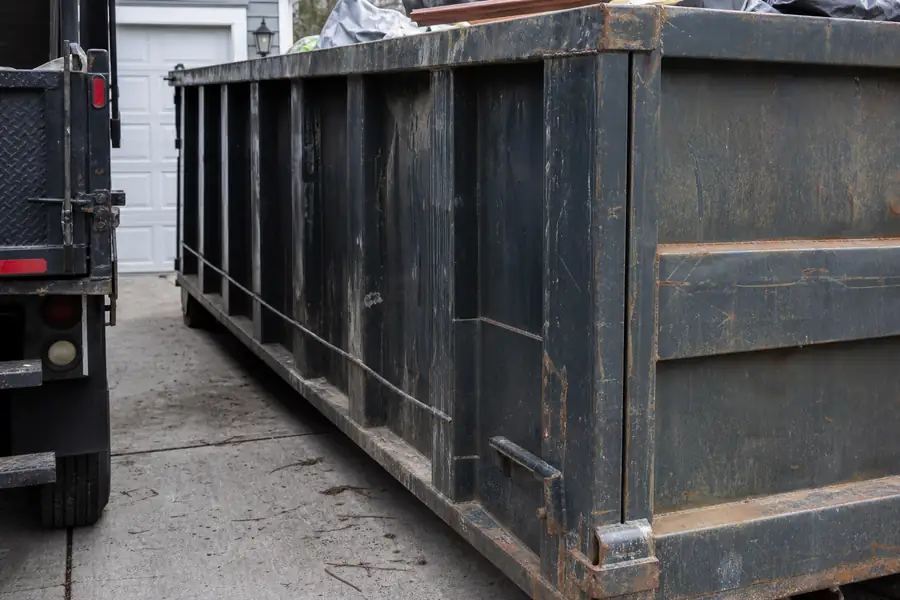 Roll-off dumpster in a driveway next to a junk removal truck